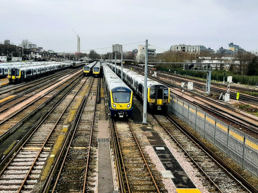 A busy railway yard featuring multiple modern London Underground trains parked on several tracks, with two trains in the foreground facing each other and additional trains lined up in the background. 